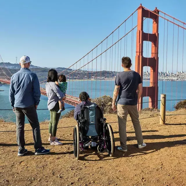 A group of people, including one person in a wheelchair, 当他们从马林海岬看金门大桥时，从背后看到的是什么.